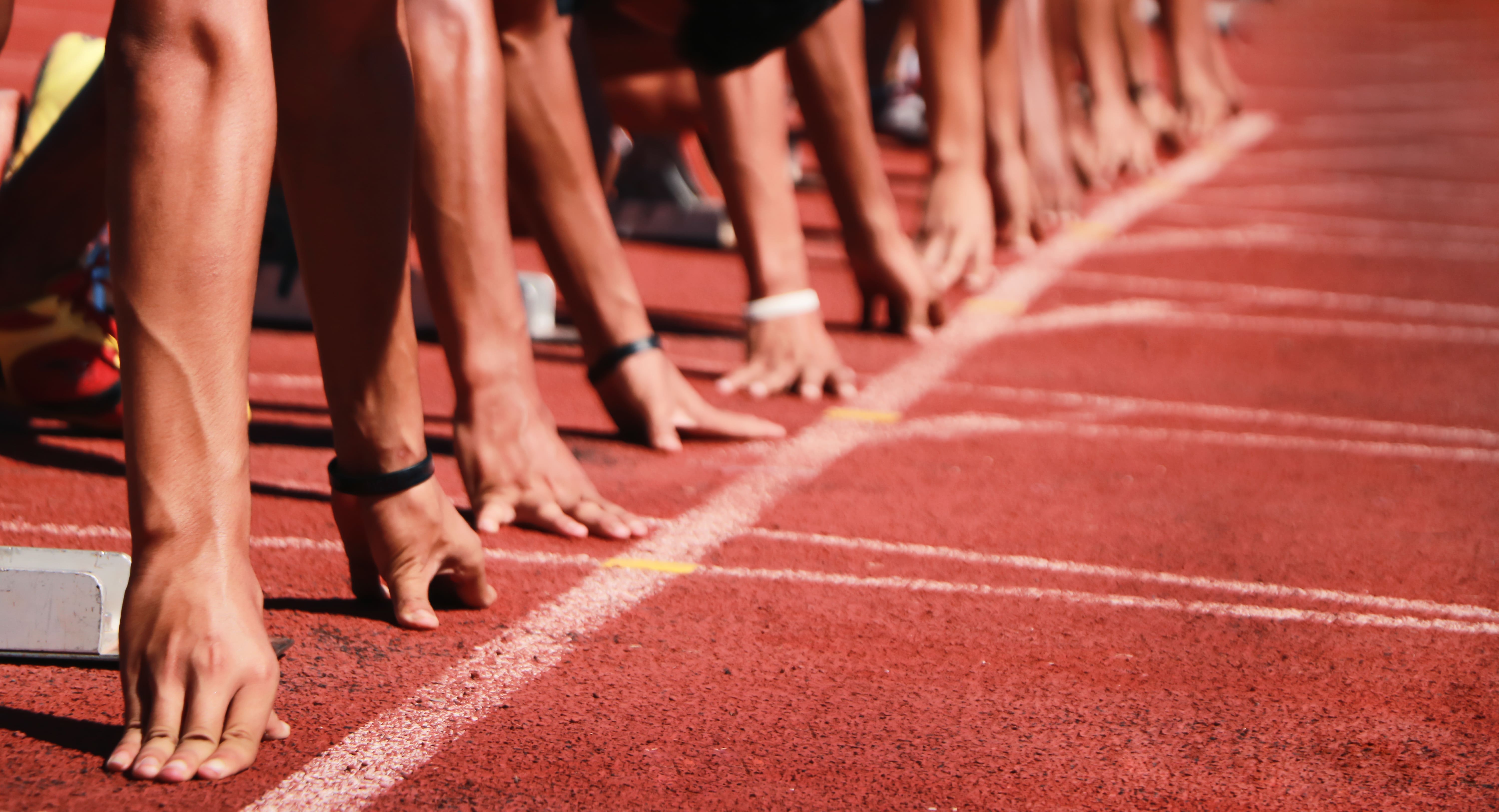 Sprinters positioned at the starting line of a red track, symbolizing readiness to launch, competitive strategy, and the drive for high performance.