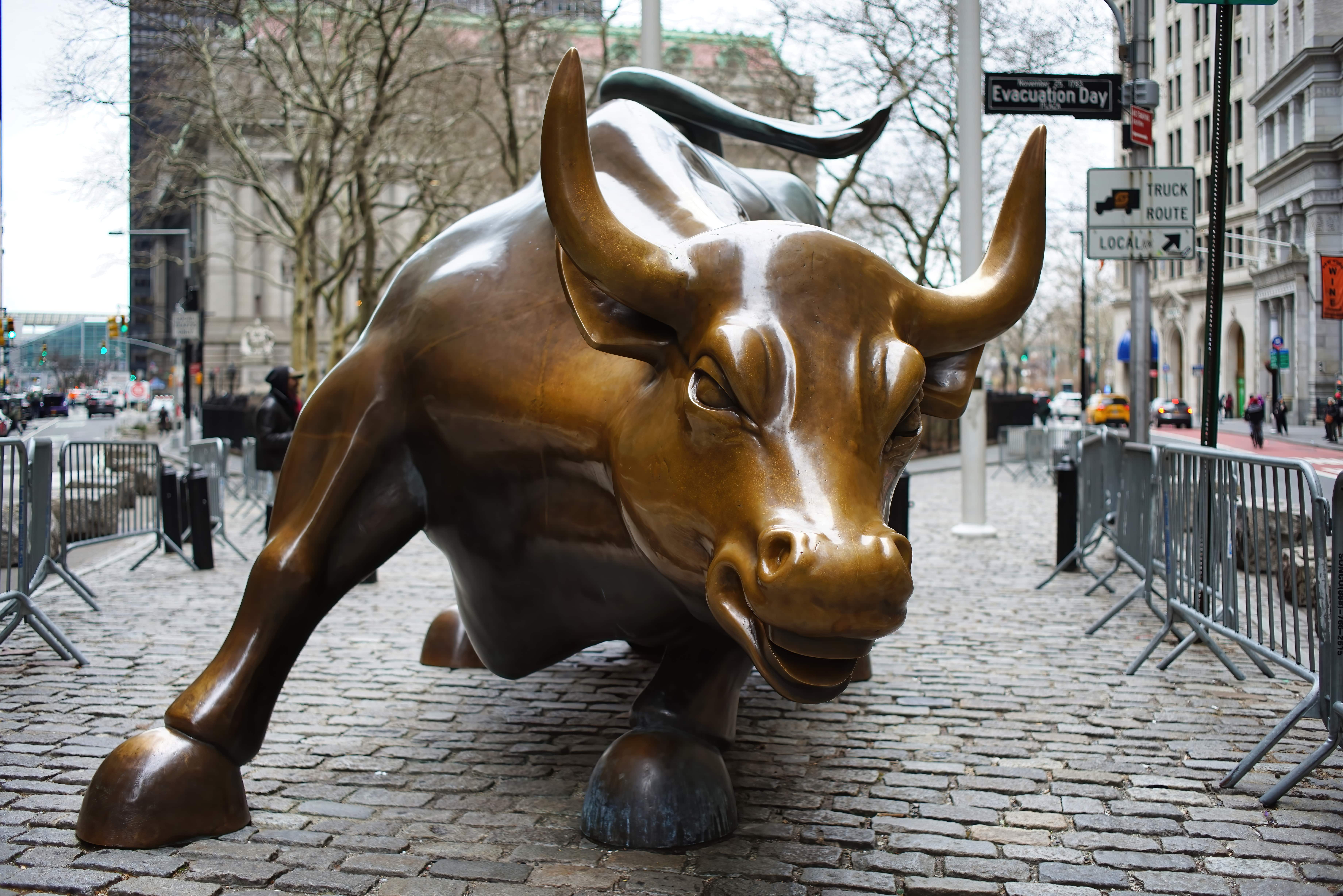 The iconic bronze Charging Bull statue standing firmly on a city street, symbolizing financial optimism, market strength, and the aggressive pursuit of economic growth on Wall Street.