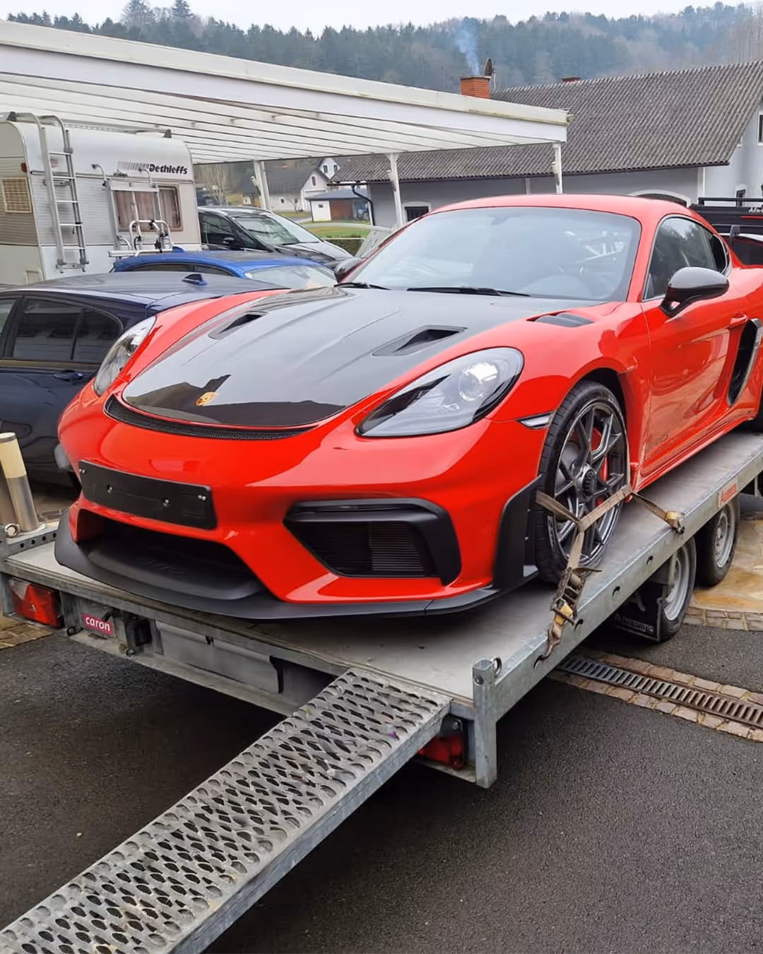 Rotes Porsche-Sportauto mit schwarzer Motorhaube gesichert auf einem Autotransporter.