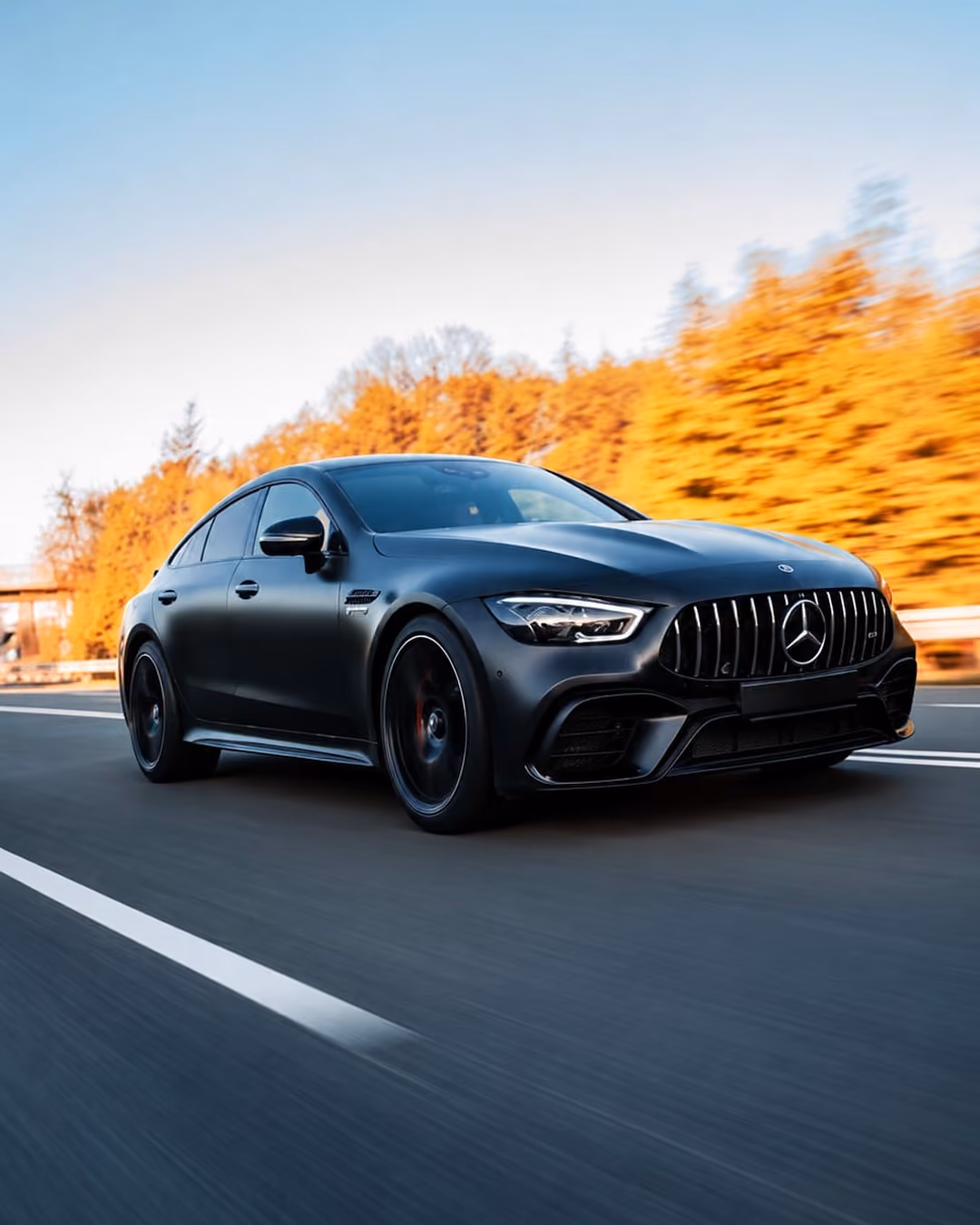 Schwarzer Mercedes-Sportwagen auf einer Straße mit herbstlich verfärbten Bäumen im Hintergrund.