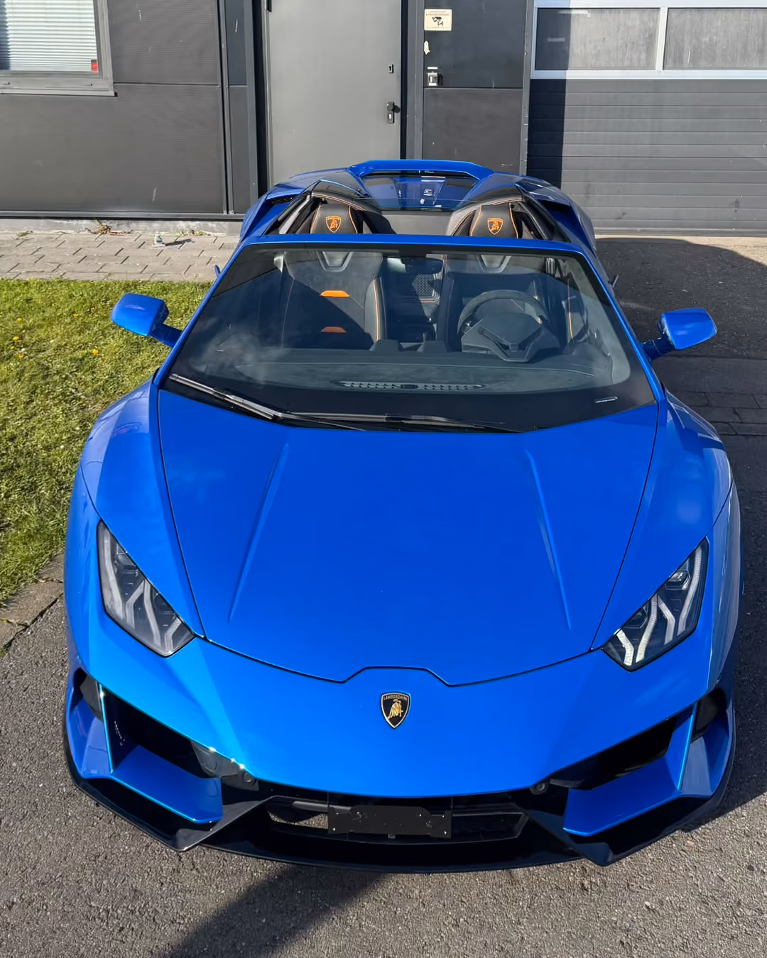 Blauer Lamborghini-Sportwagen mit offenem Verdeck, von vorne fotografiert vor einem Gebäude.