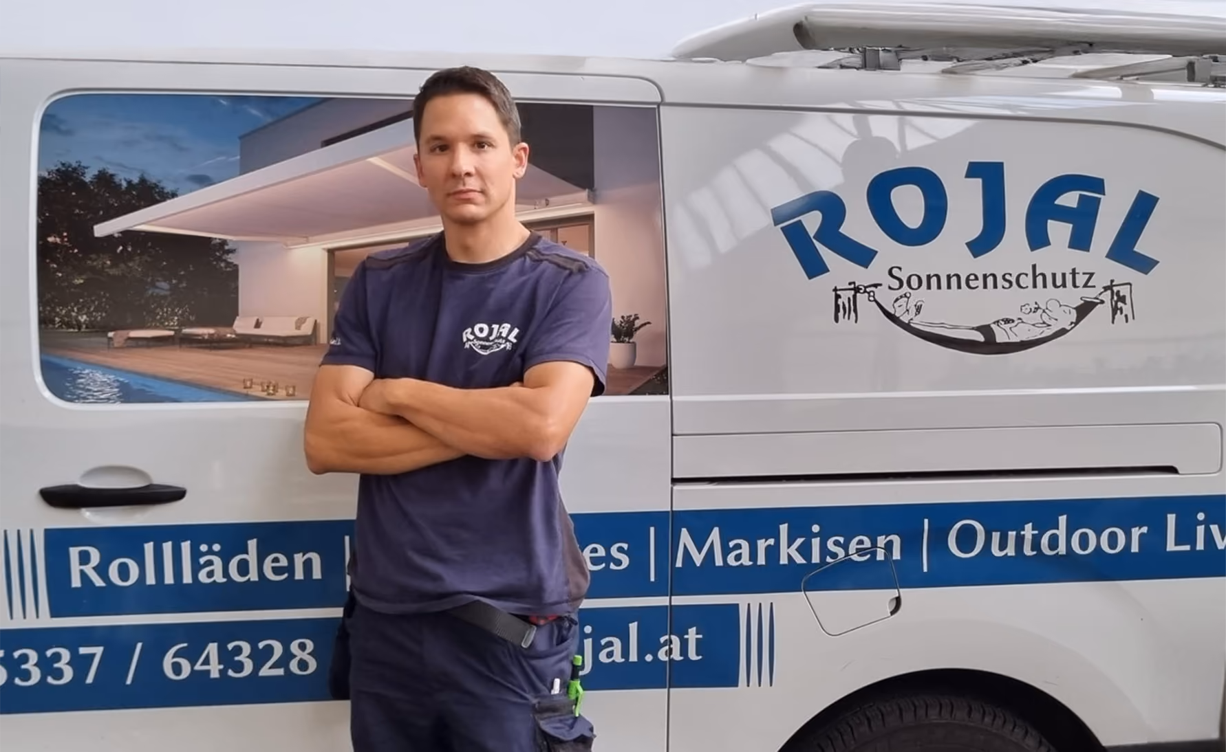Mann in blauem T-Shirt mit verschränkten Armen steht vor einem weißen Firmenwagen mit ROJAL Sonnenschutz-Logo.
