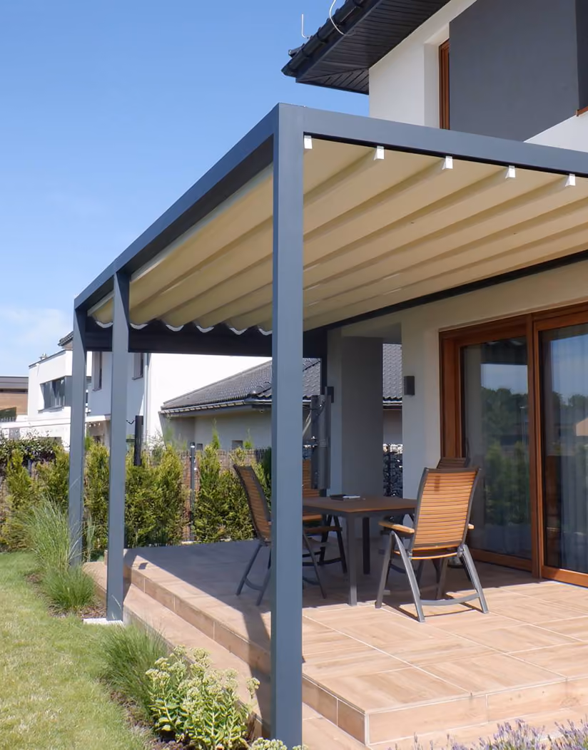 Moderne Terrasse mit Pergola, Tisch und Holzstühlen vor einem weißen Haus mit Fliesenboden.