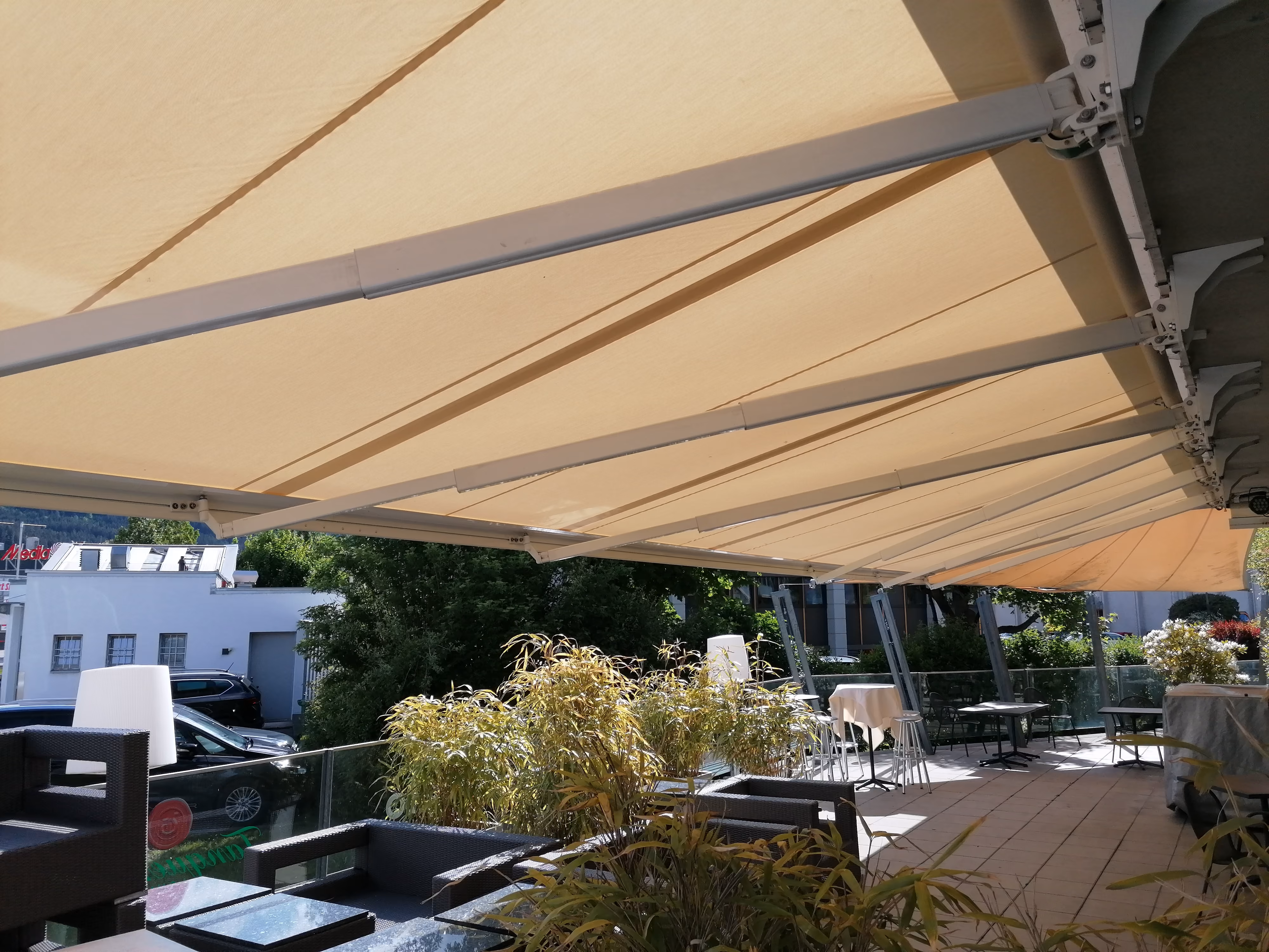 Sonnige Terrasse mit ausfahrbarer Markise, Gartenmöbeln und Pflanzen auf Fliesenboden.