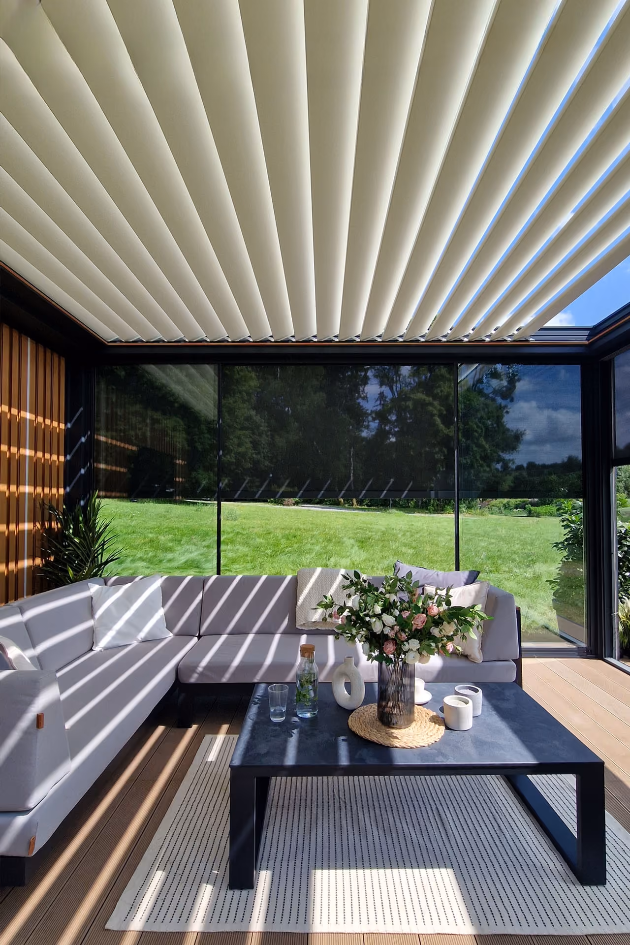 Moderne Terrasse mit grauem Ecksofa, schwarzem Tisch und weißen dekorativen Elementen.
