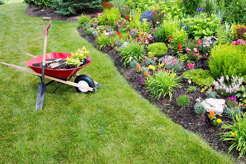 Lawn with a bed of flowers and a wheelbarrow with mulch in Monroe and Surrounding Counties