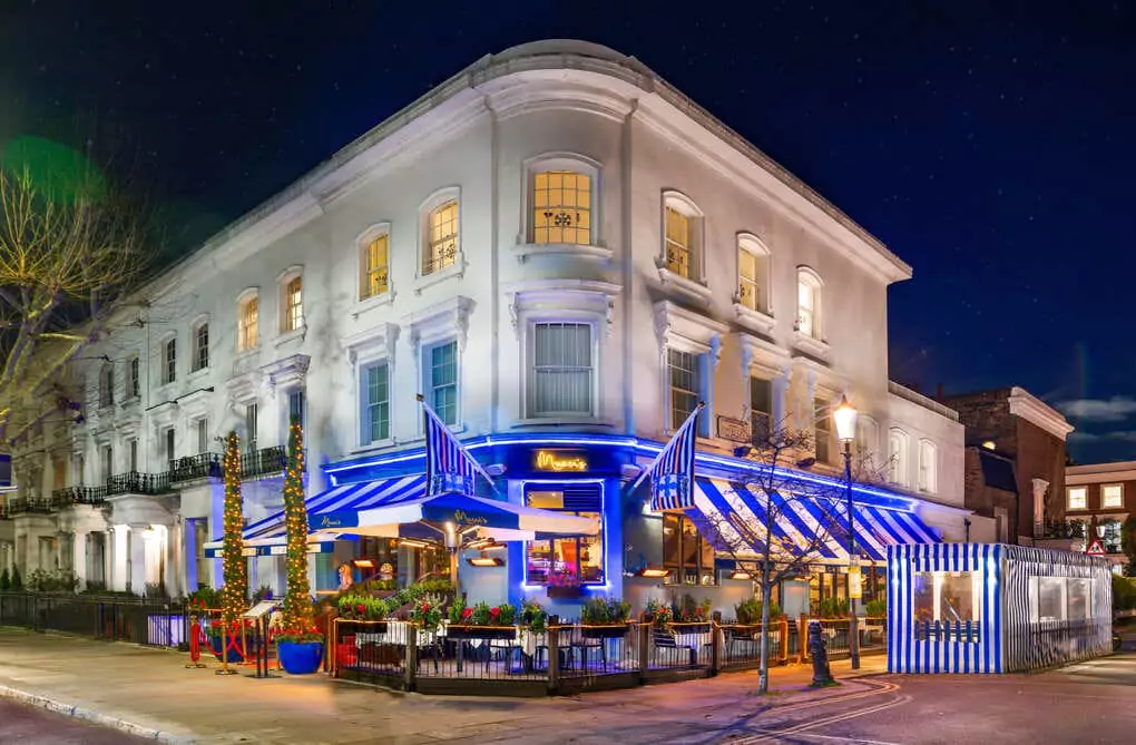 A gourmet lasagna dish being freshly seasoned with black pepper, served with a glass of red wine at an upscale Chelsea restaurant. Discover the best dining spots in Chelsea with Ambl for last-minute reservations.