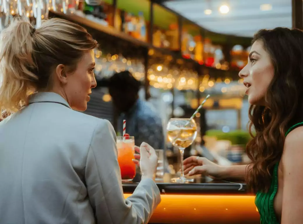 Two women engaging in conversation over cocktails at an Ambl-listed venue, enjoying a seamless booking experience.