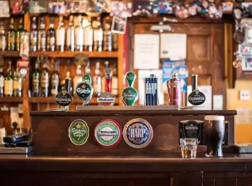 A classic pub bar featuring an array of beer taps, whiskey bottles, and a cozy atmosphere, showcasing one of the many traditional venues users can discover through the Ambl app.
