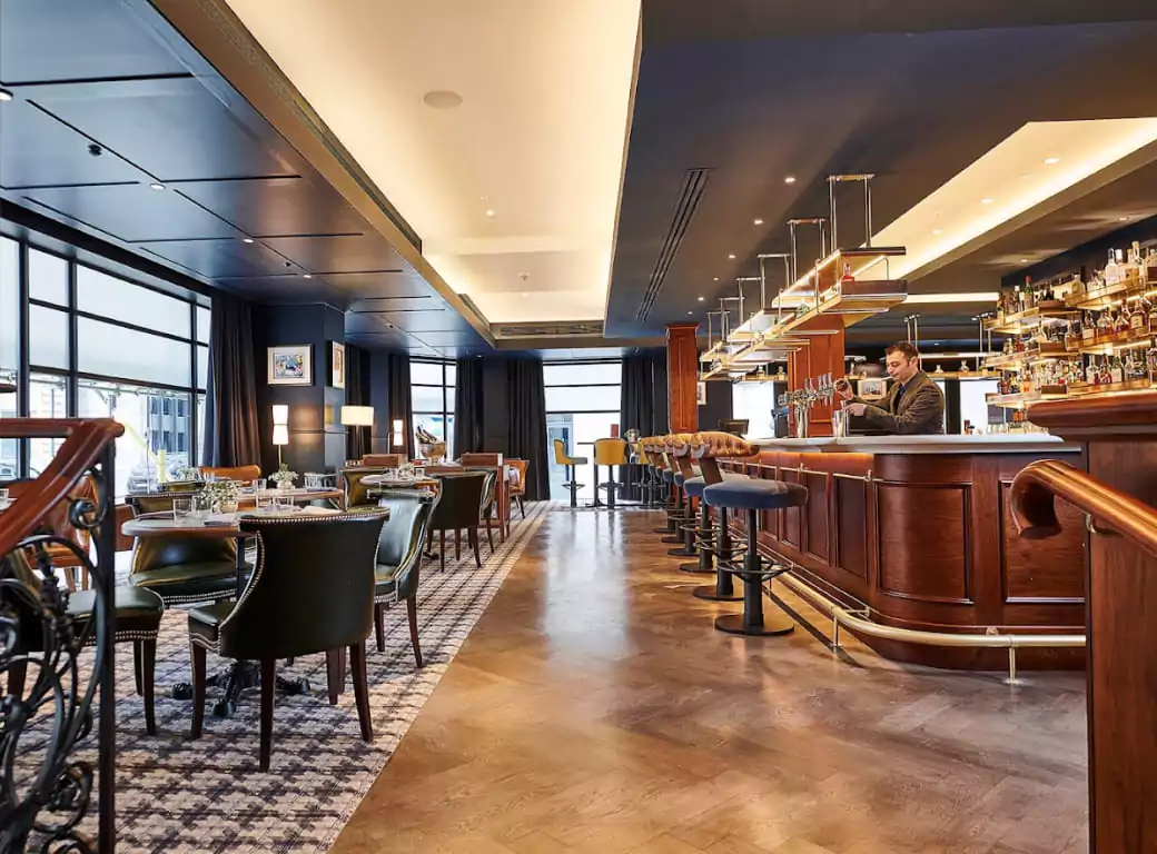 A stylish, upscale bar and dining area with elegant seating and a bartender preparing drinks, representing the premium bar experiences available for instant booking on Ambl.
