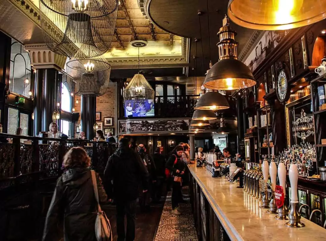 An elegant pub with ornate chandeliers, a long bar, and a bustling atmosphere, highlighting Ambl’s selection of must-visit historic venues.