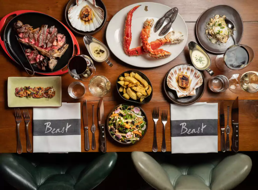 A luxurious dining spread featuring premium steak, king crab legs, scallops, truffle fries, and fresh salad at Beast, a high-end restaurant. One of the top Ambl-listed venues for an unforgettable steak and seafood experience.