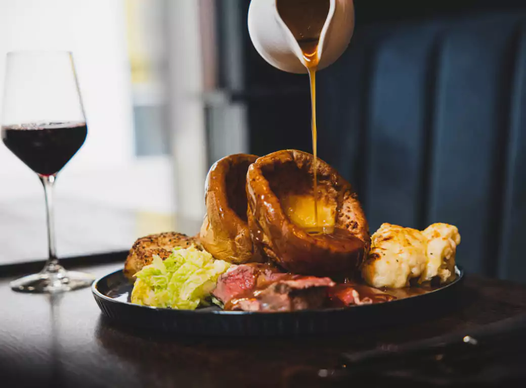 A mouthwatering Sunday roast with Yorkshire puddings, tender roast beef, greens, and cauliflower cheese, topped with rich gravy. One of the best Ambl-recommended spots for a traditional British dining experience.