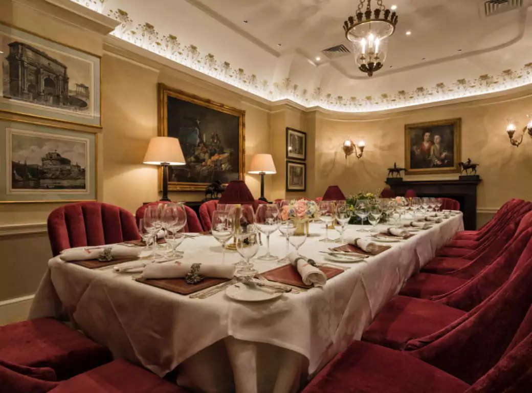 A luxurious private dining room with an elegantly set long table, plush red velvet chairs, and classic artwork, offering an exclusive space for group bookings and special events. Available for reservations through the Ambl app.