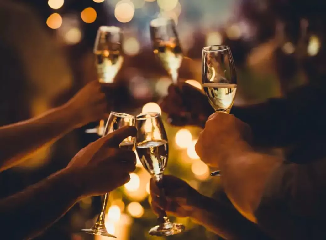 A group of friends raising champagne glasses in a celebratory toast, surrounded by warm glowing lights celebrating in a venue available for last-minute booking through the Ambl app.