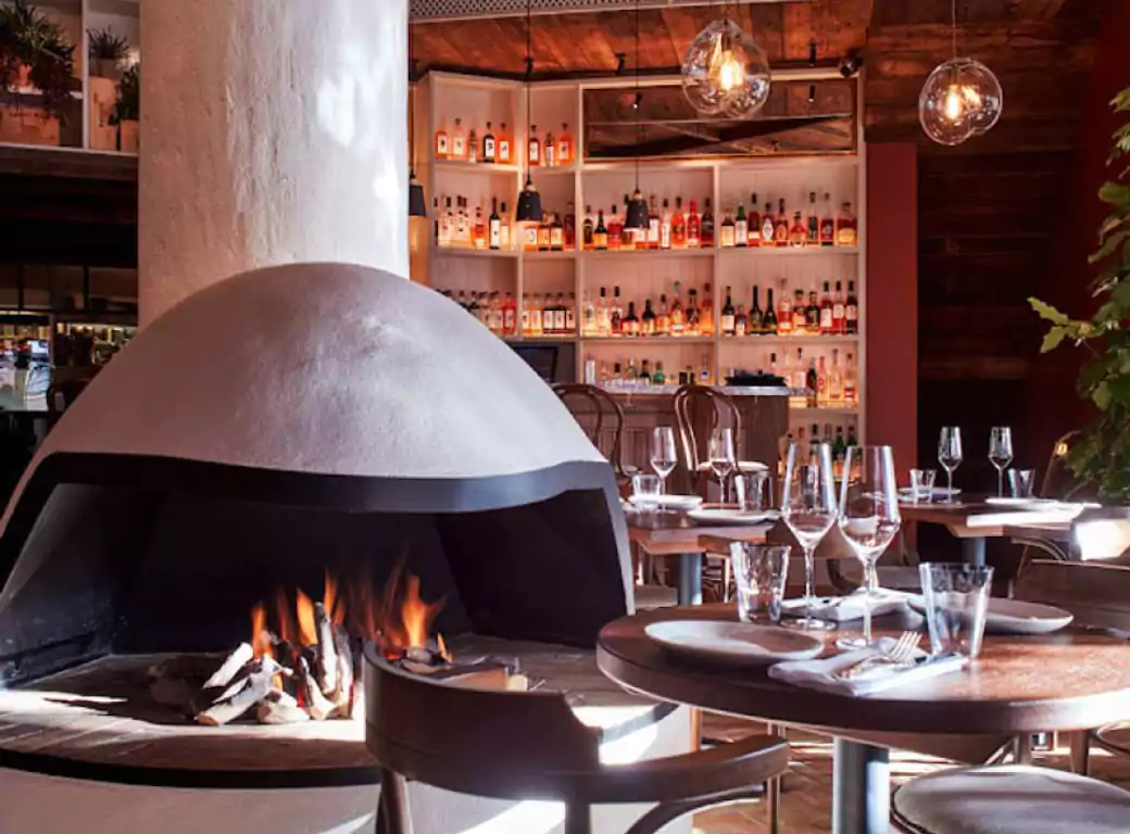 A cozy and stylish restaurant with a warm open fireplace, elegant table settings, and a well-stocked bar, creating the perfect intimate dining experience. One of the hidden gems discoverable through the Ambl app.