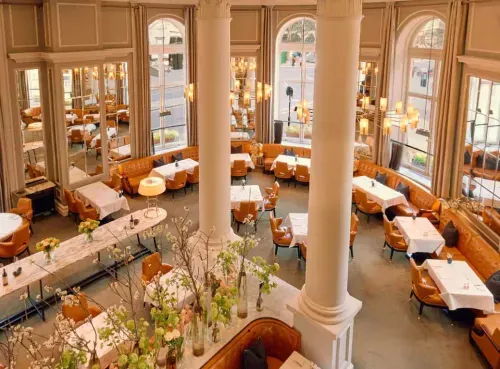 A stunning pre-theatre dining venue with grand columns, high ceilings, and elegant chandeliers, offering a refined ambiance for a luxurious meal before the show. Discover top pre-theatre restaurants in London with Ambl.
