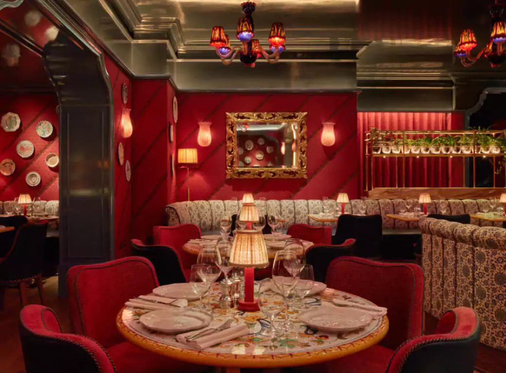 A romantic and intimate restaurant with plush red seating, warm lighting, and elegant table settings—perfect for a date night in London. Find the best date night spots with Ambl.