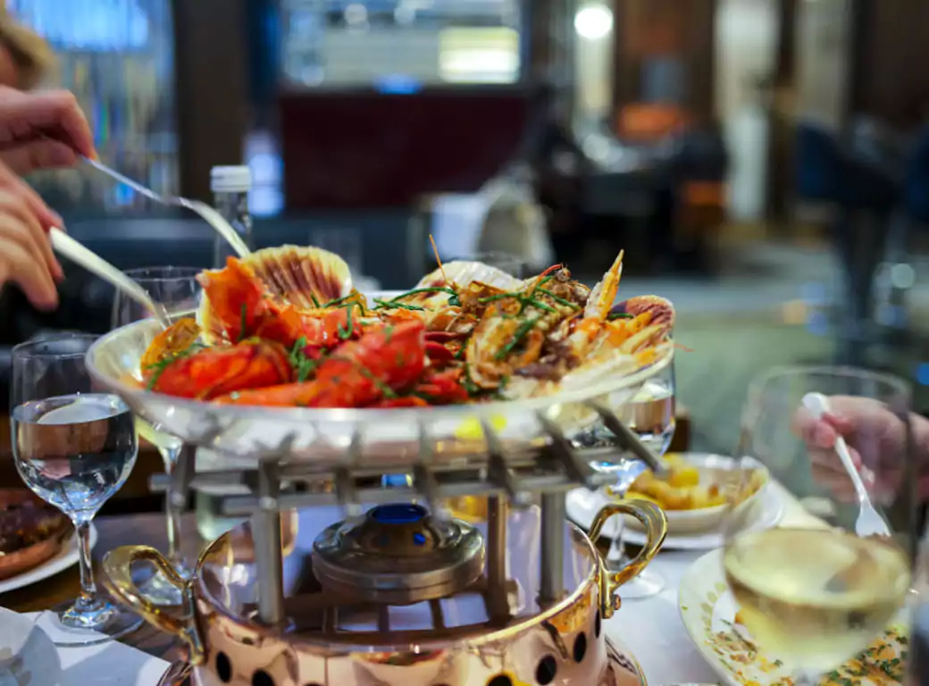 A luxurious seafood platter featuring lobster, scallops, and shellfish, served over a flame at an upscale London restaurant. Find last-minute dining experiences like this with Ambl.