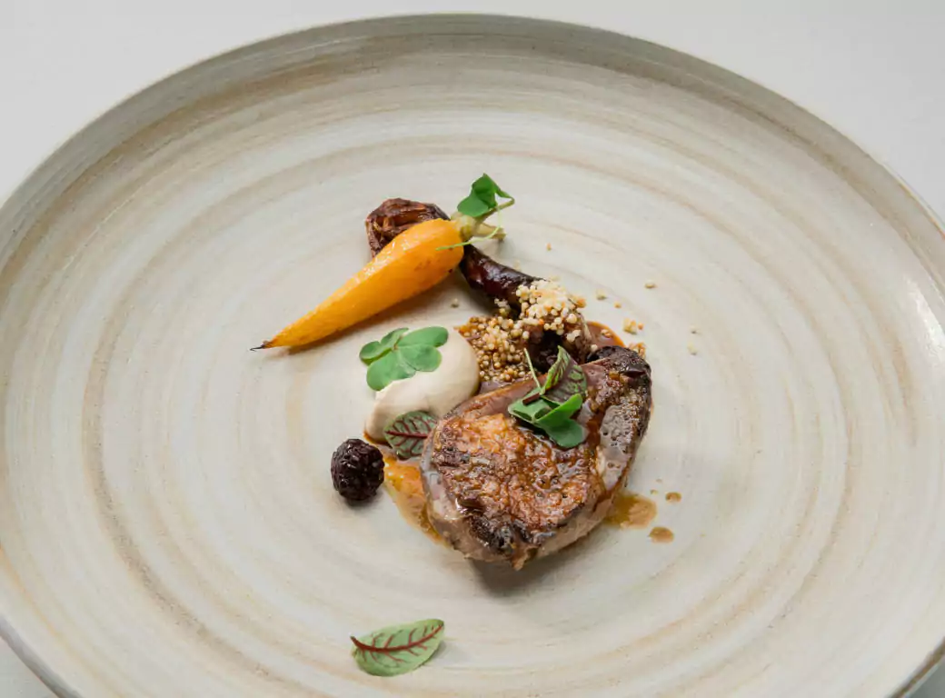 A beautifully plated Michelin-star dish featuring a perfectly seared cut of meat, delicate vegetables, and artistic garnishes on a minimalist ceramic plate. Discover fine dining with Ambl.