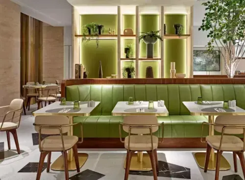 A stylish modern restaurant with fresh green and gold décor, perfect for a business lunch. Sleek tables, comfortable seating, and elegant lighting create a sophisticated yet inviting atmosphere. Ideal for networking, meetings, or client dining, discover top business lunch spots with Ambl.