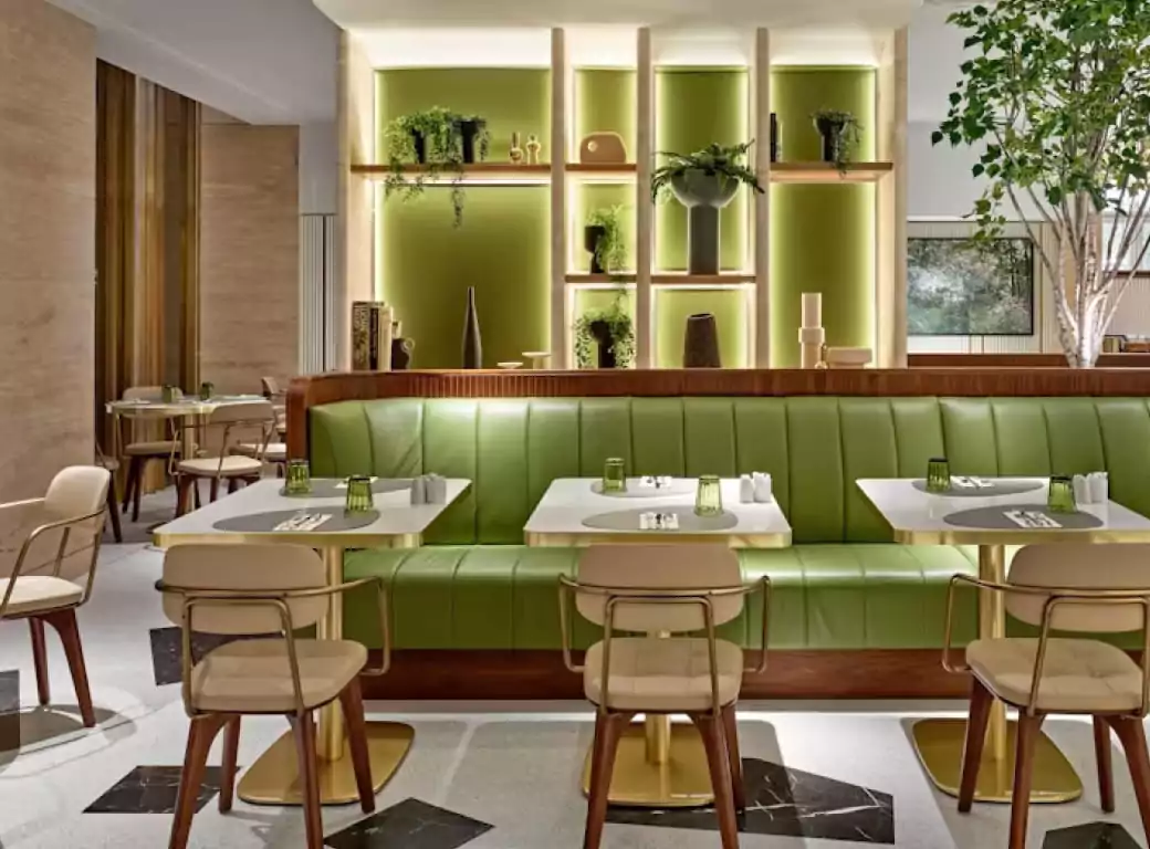 A stylish modern restaurant with fresh green and gold décor, perfect for a business lunch. Sleek tables, comfortable seating, and elegant lighting create a sophisticated yet inviting atmosphere. Ideal for networking, meetings, or client dining, discover top business lunch spots with Ambl.