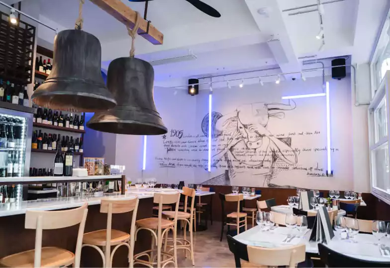 A modern restaurant with rustic wooden furniture, oversized hanging bells, and a mural on the wall. The perfect setting for a cozy meal with an artistic touch. Find top dining spots like this on Ambl.
