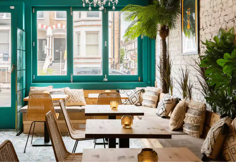 A cozy and bohemian café with teal walls, wooden furniture, and tropical plants, creating a relaxed atmosphere. Explore unique cafés in London with Ambl.