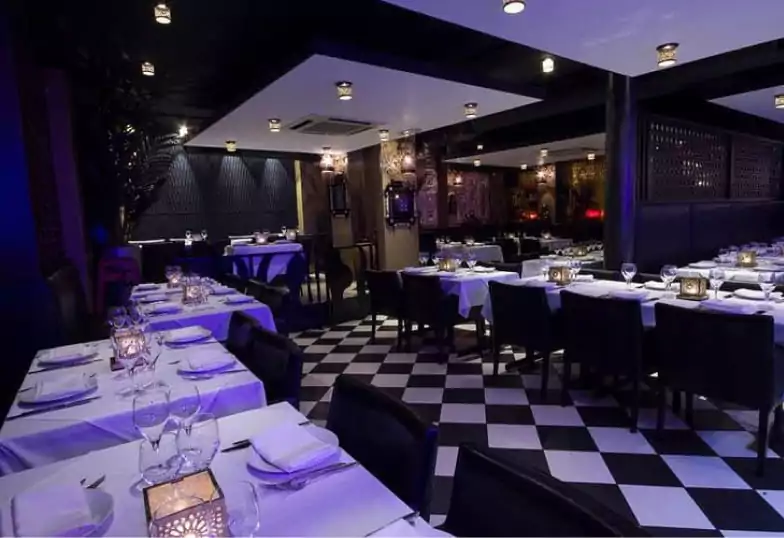A sophisticated restaurant with a black-and-white checkered floor, luxurious dining tables, and dim, ambient lighting. Let Ambl guide you to the best fine dining spots in London.