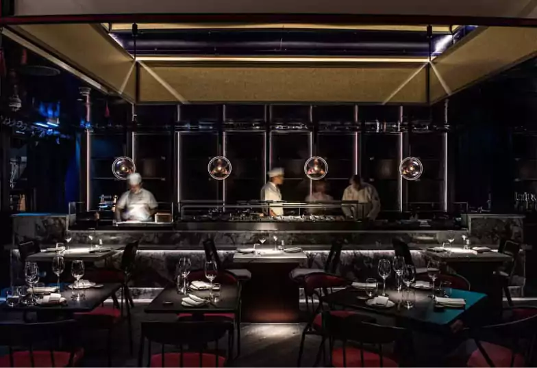 A sleek and modern Japanese restaurant with a dark interior, an open kitchen concept, and stylish lighting. Experience exceptional dining in London with Ambl.