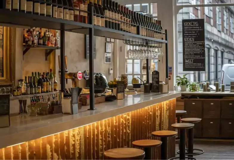 A rustic yet modern bar with a long counter, stylish wooden stools, and hanging wine bottles, a perfect spot to discover with Ambl.