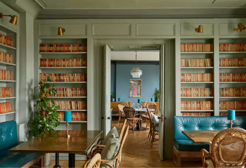 A cozy and literary-inspired dining space at Bingham, with walls lined with books and charming vintage furnishings. Discover unique dining spaces with Ambl.