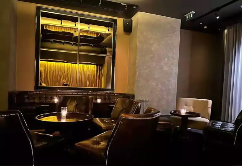 A sleek and moody cocktail lounge with plush leather seating, warm golden lighting, and a refined ambiance at Blind Spot. Discover stylish hidden bars like this with Ambl.