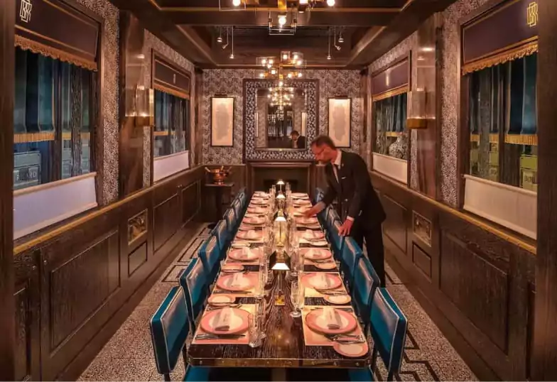 An intimate private dining room with a long table, luxurious blue velvet chairs, and dark wood paneling at Bob Bob Ricard. Find exclusive dining experiences like this with Ambl.