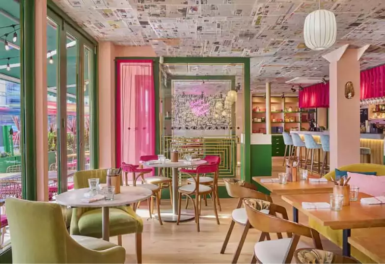 A luxurious Indian restaurant with warm amber lighting, intricate carved décor, and an ornate mirror reflecting the stylish bar. Chandeliers cast a soft glow over the elegant seating and attentive staff. Experience the rich flavors and opulence of Indian cuisine with Ambl.