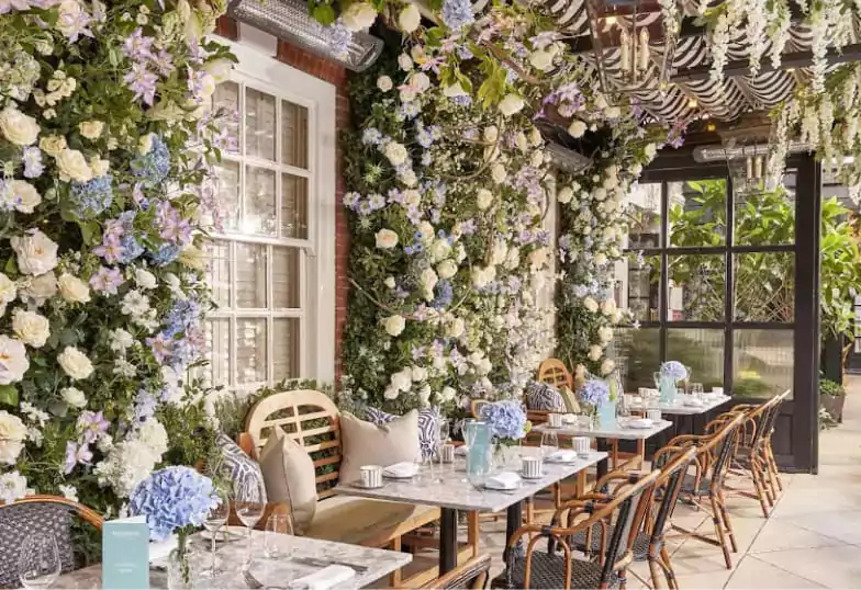 A floral-filled outdoor terrace with charming bistro-style seating, bathed in soft natural light, perfect for elegant alfresco dining with Ambl.