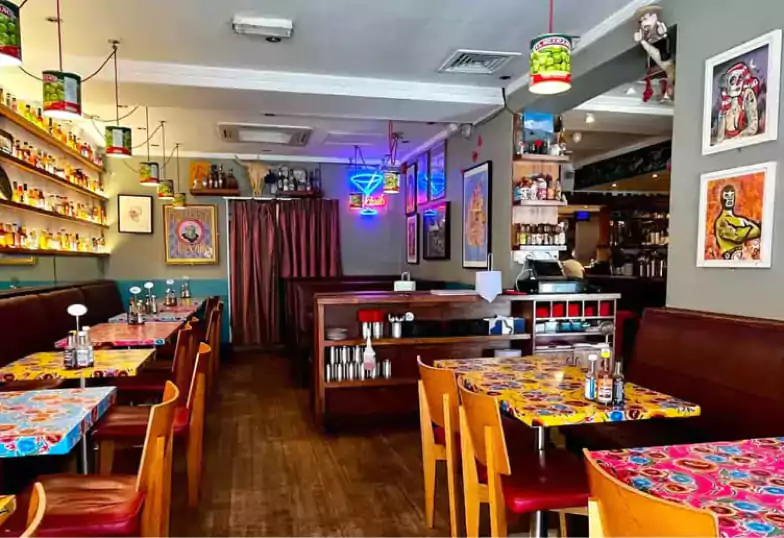 A lively and colorful Mexican eatery with vibrant table designs, neon signage, and shelves filled with an array of hot sauces, bringing energy and authenticity with Ambl.