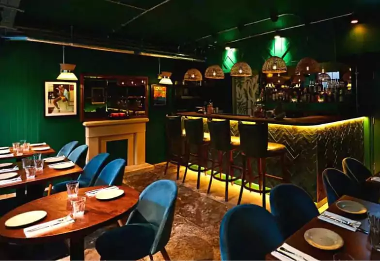 A stylish bar and dining space with deep green walls, dim lighting, and a golden glow, offering an intimate setting for modern cuisine with Ambl.