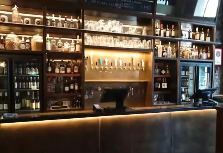 A well-stocked, dimly lit bar with an industrial-chic design, featuring a wide selection of spirits and craft beers. An intimate setting for cocktails and conversation. Find more stylish bars like this on Ambl.