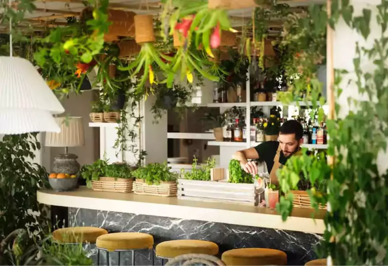 A tropical-themed cocktail bar with lush hanging greenery, rattan light fixtures, and a marble counter, serving fresh botanical cocktails. A serene escape in the city. Find more botanical bars on Ambl.