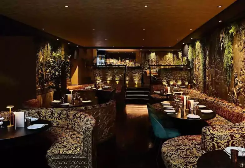 An exotic lounge and dining venue with ornate carved walls, rich gold tones, and ambient candlelight, offering a lavish and immersive experience. A hidden gem for luxury dining. Find more opulent spaces on Ambl.