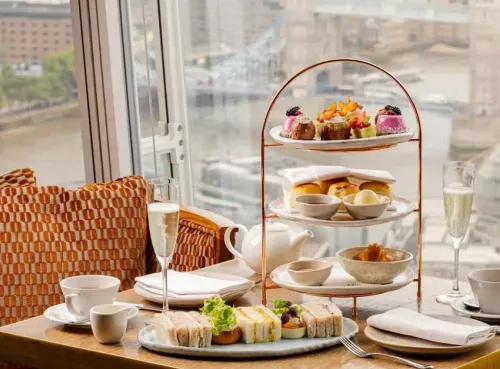 A beautifully presented afternoon tea setup featuring a tiered tray with freshly baked scones, pastries, and desserts, accompanied by tea and condiments. One of the luxurious dining experiences available through the Ambl app.
