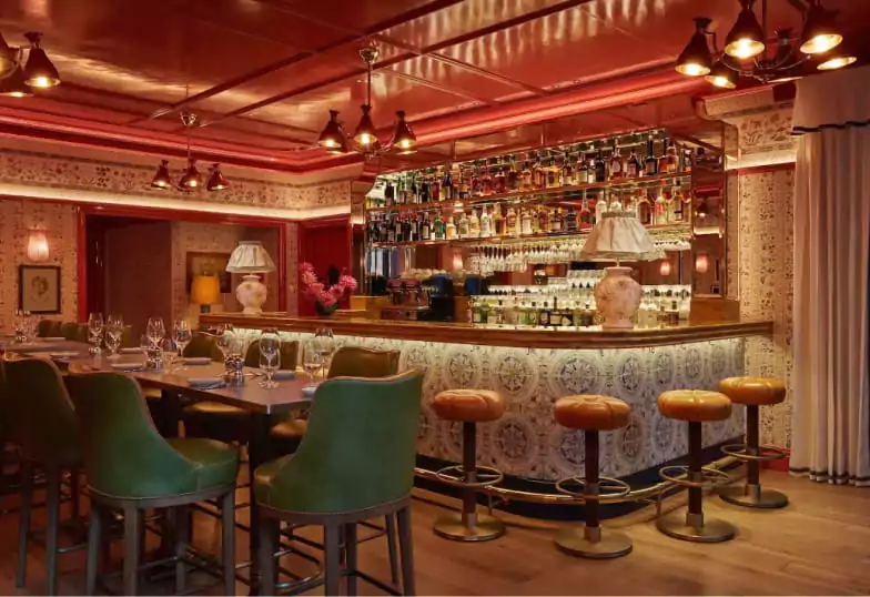 A chic speakeasy-style bar with warm lighting, emerald green bar stools, and a cozy, vintage atmosphere, bookable on Ambl.