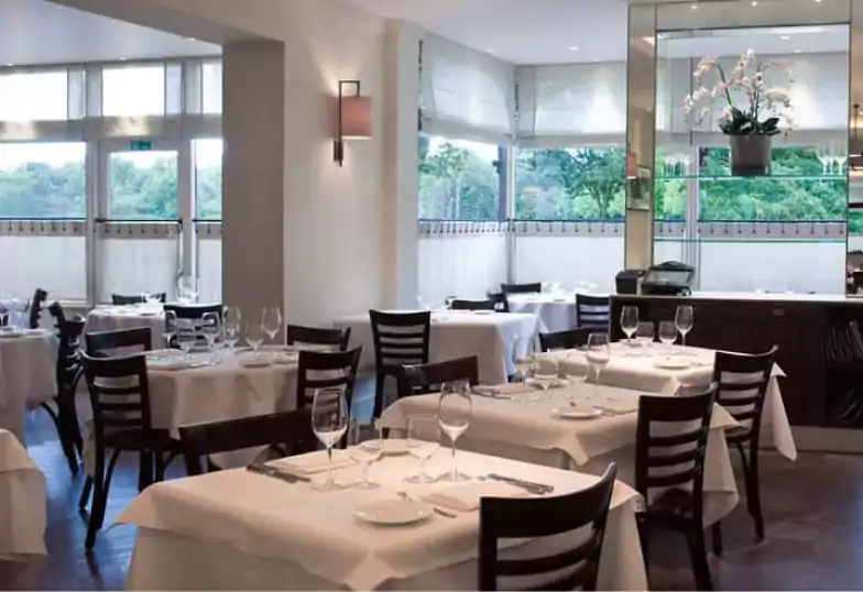 A refined and classic restaurant with elegant white table settings at Chez Bruce. Find exquisite dining like this with Ambl.