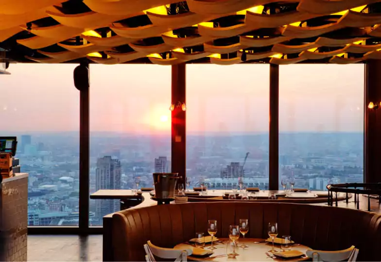 A high-rise restaurant with a stunning cityscape view at sunset, featuring contemporary decor and warm ambient lighting with Ambl.