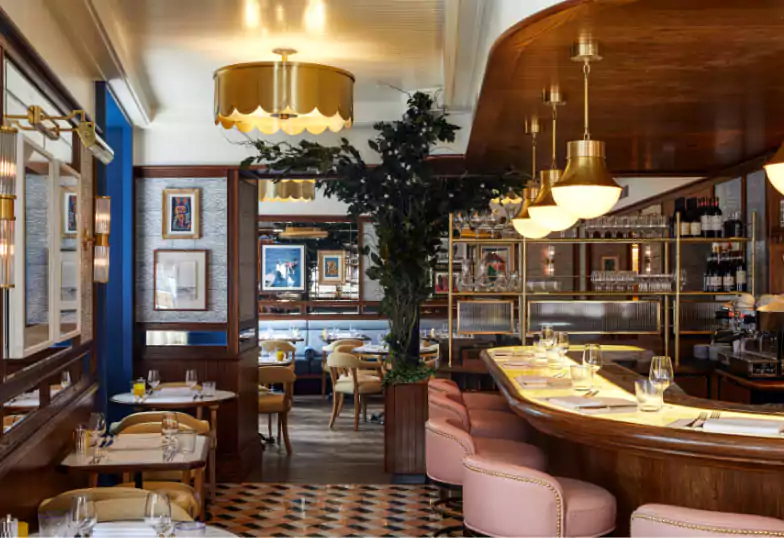 A classic Italian-style restaurant at Chucs Mayfair, featuring a luxurious curved bar, plush pink stools, and golden lighting accents. Discover timeless elegance with Ambl.