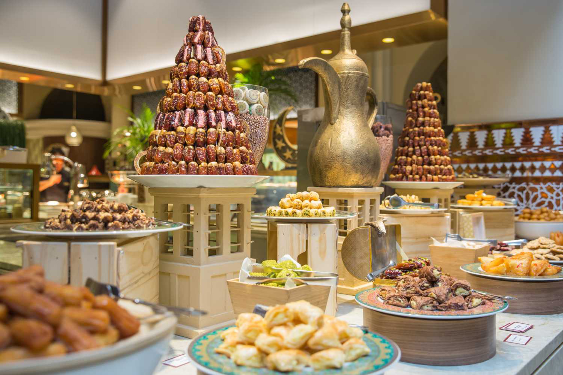 Cozy Ramadan Iftars in Dubai, think Arabic lanterns, dates, lentil soup and sharing dishes, set against a warm, low-lit restaurant backdrop.