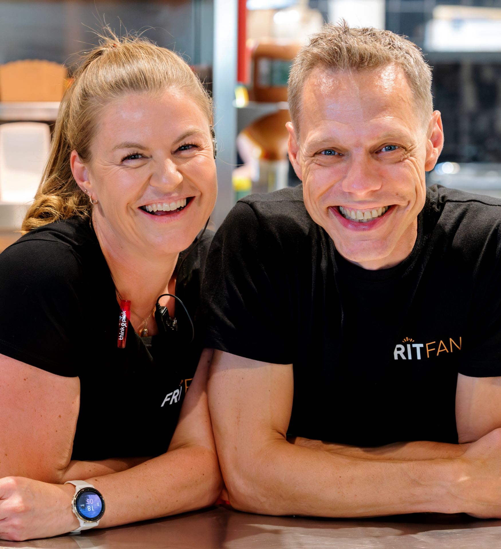 Twee lachende mensen in sportkleding poseren in een keuken.
