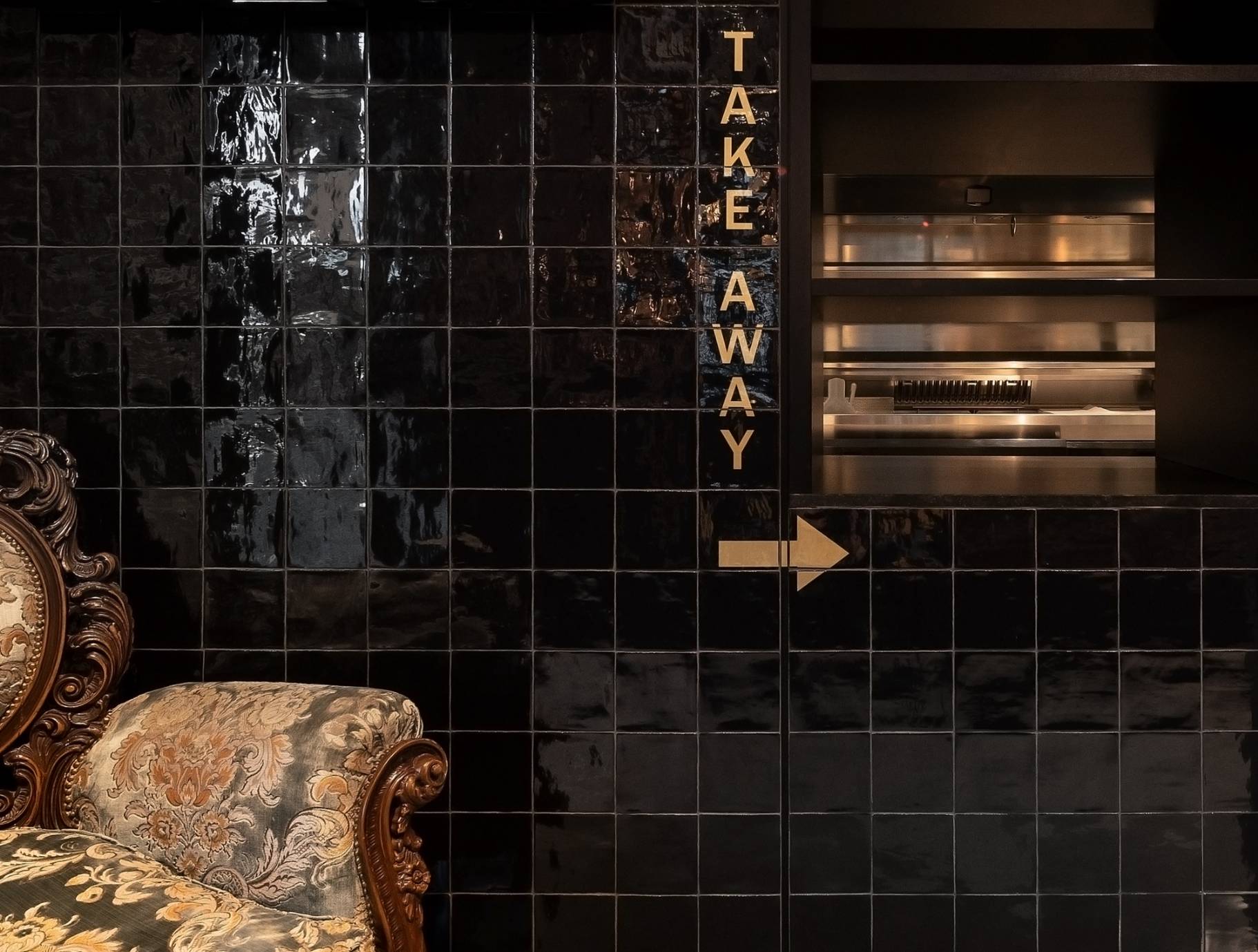 Zwart betegelde muur met "Take Away" bord en antieke stoel.