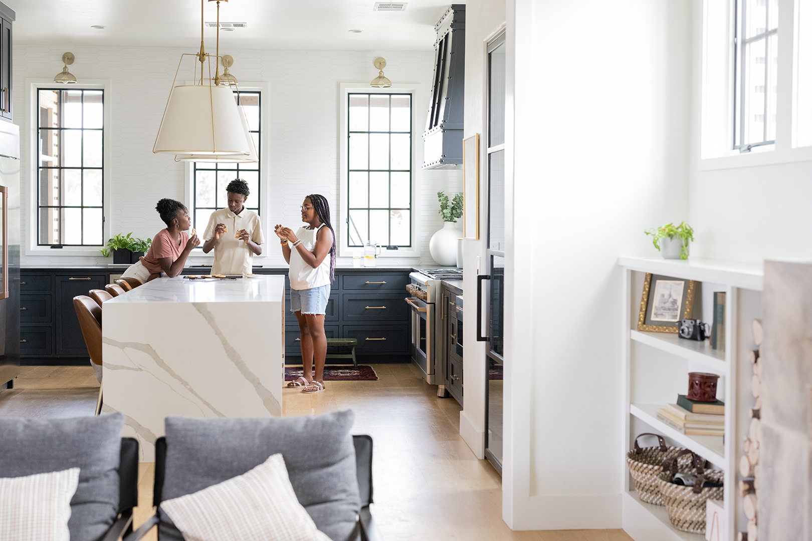 Three people standing and eating together at a modern kitchen island with white marble countertop and black cabinetry.